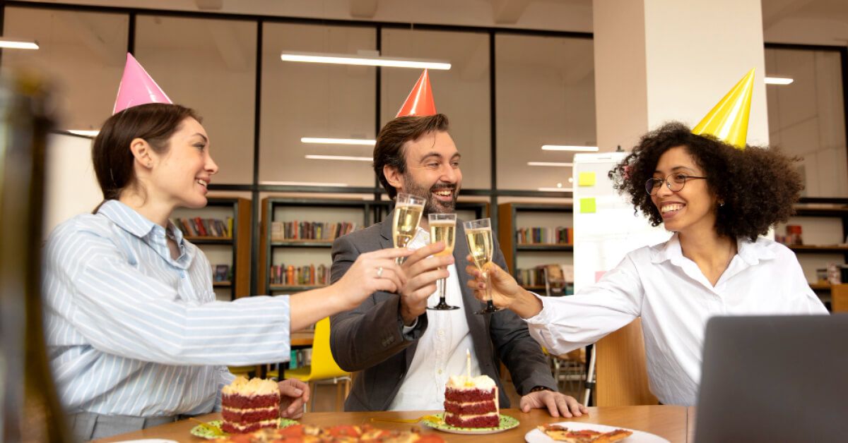 Employees are celebrating a party in the workplace with cake and wine