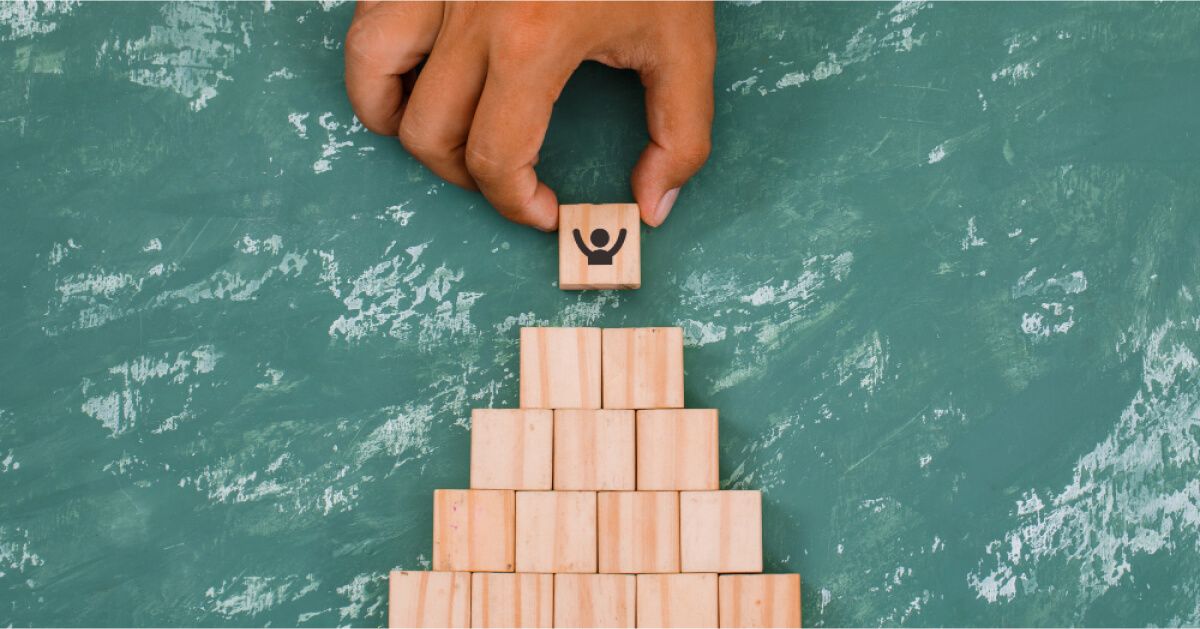 Someone placing a wooden block with an employee graphic on top of a tower of blocks