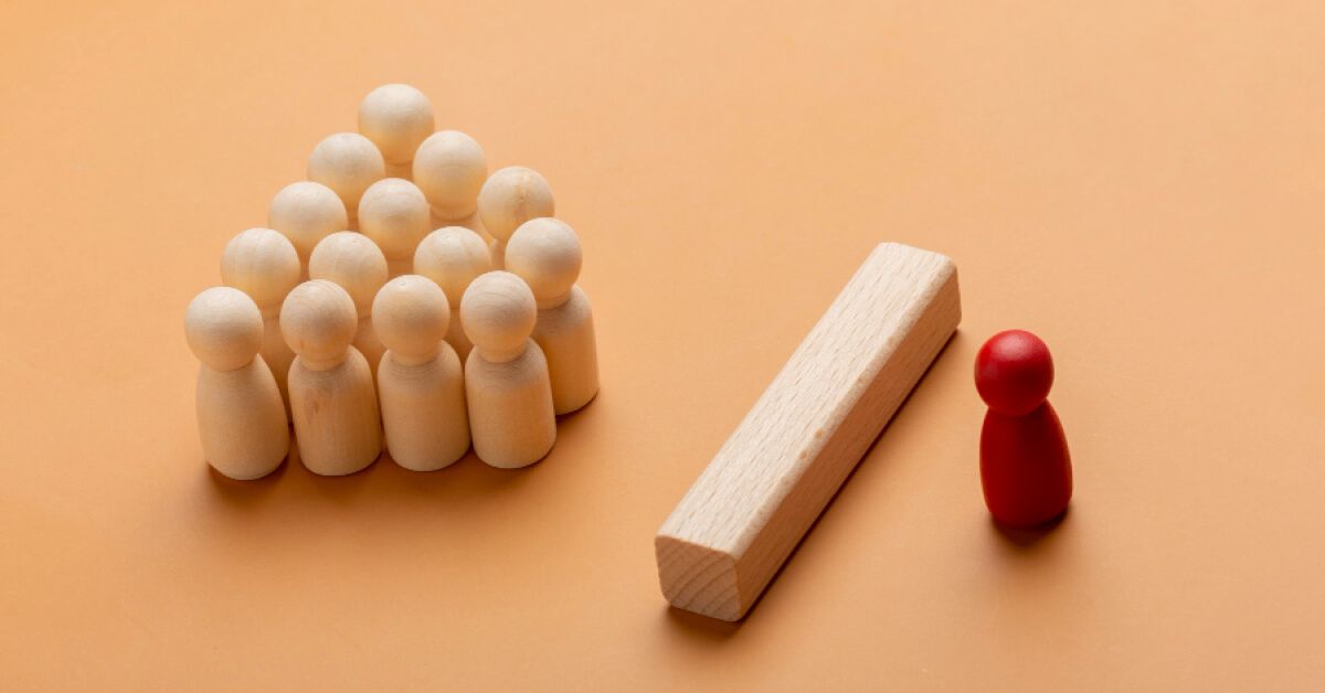 Red pawn separated by a wooden block from a group of white pawns