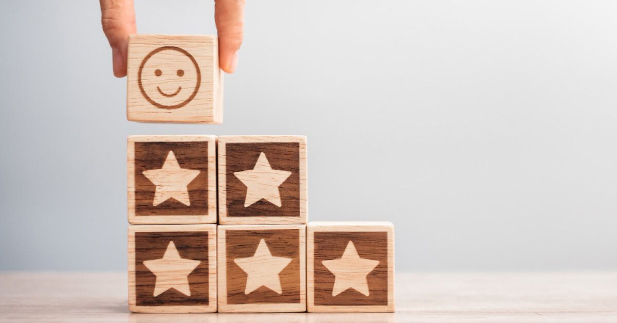 Person placing a wooden block with emoticon on top of a set of wooden blocks arranged like steps