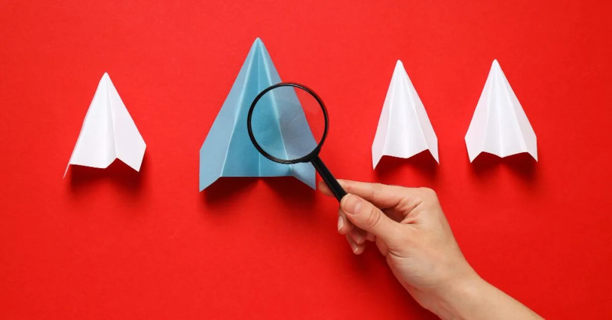 Magnifier glass pointed over a grey paper airplane